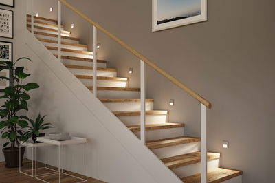 Moderne houten trap met witte treden en warmwitte LED-wandlampen voor sfeervolle trapverlichting