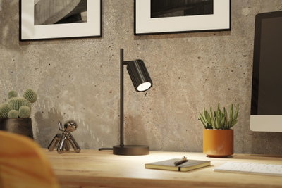 Schwarze Metall-Tischlampe mit geriffeltem Lampenschirm auf Holzschreibtisch mit Dekoration und Monitor