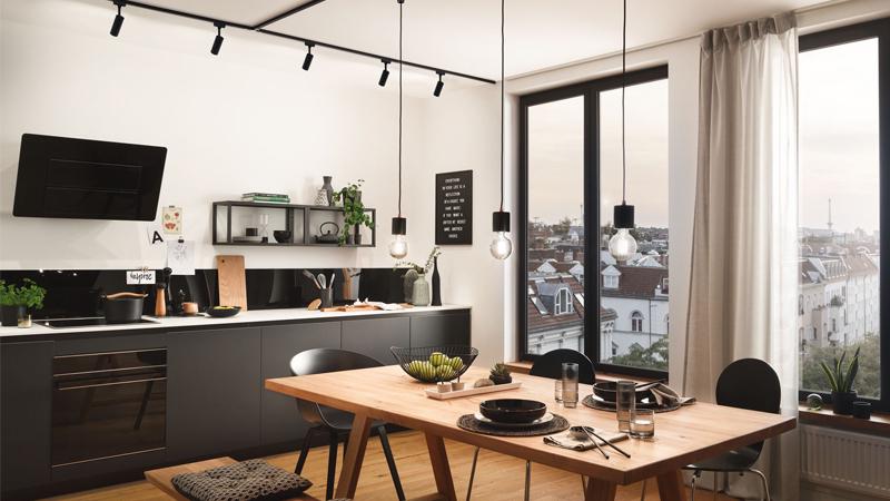 Moderne Küche mit schwarzen Hängelampen, Holztisch und großem Fenster mit Stadtblick, LED Beleuchtung