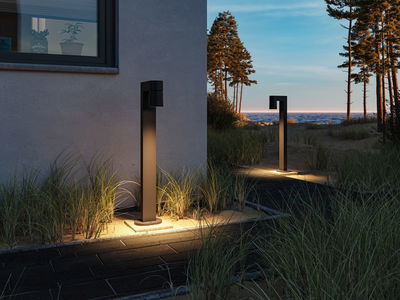 Modern black metal outdoor light illuminating garden path at dusk with sea view.