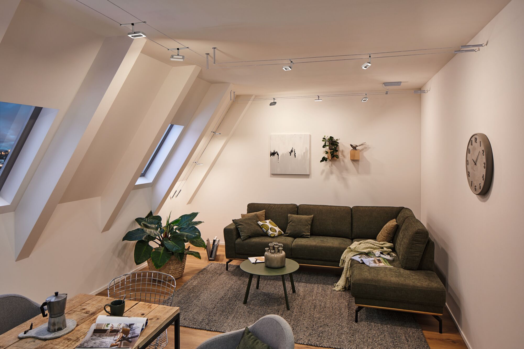 Moderne woonkamer met groene stoffen bank, grijs vloerkleed en minimalistische metalen plafondverlichting.