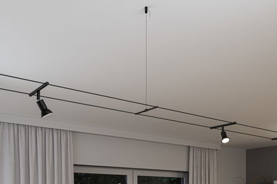 Black minimalist cable lighting system with two adjustable spotlights on white ceiling for modern room lighting