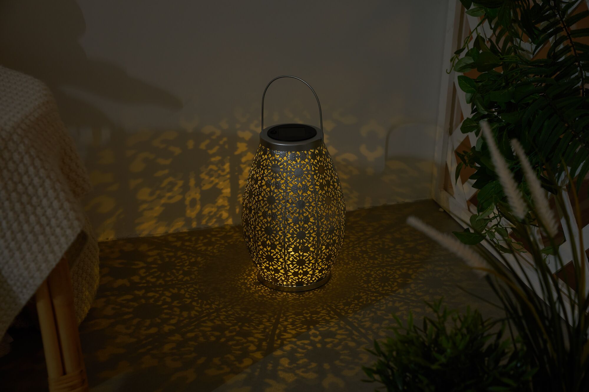 Lanterne en métal gris foncé avec motif fin, diffusant une lumière chaude et des ombres décoratives.
