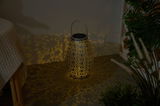 Dark grey metal lantern with intricate pattern casting warm light and decorative shadows indoors.