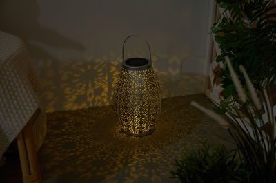 Dark grey metal lantern with intricate pattern casting warm light and decorative shadows indoors.