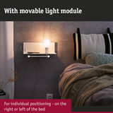 White wall lamp with movable light module and shelf next to bed with grey wall and cushions