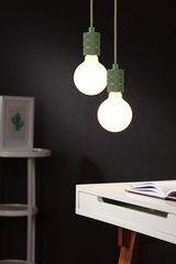 Two hanging LED bulbs with green metal sockets above white desk with open book, modern lighting.