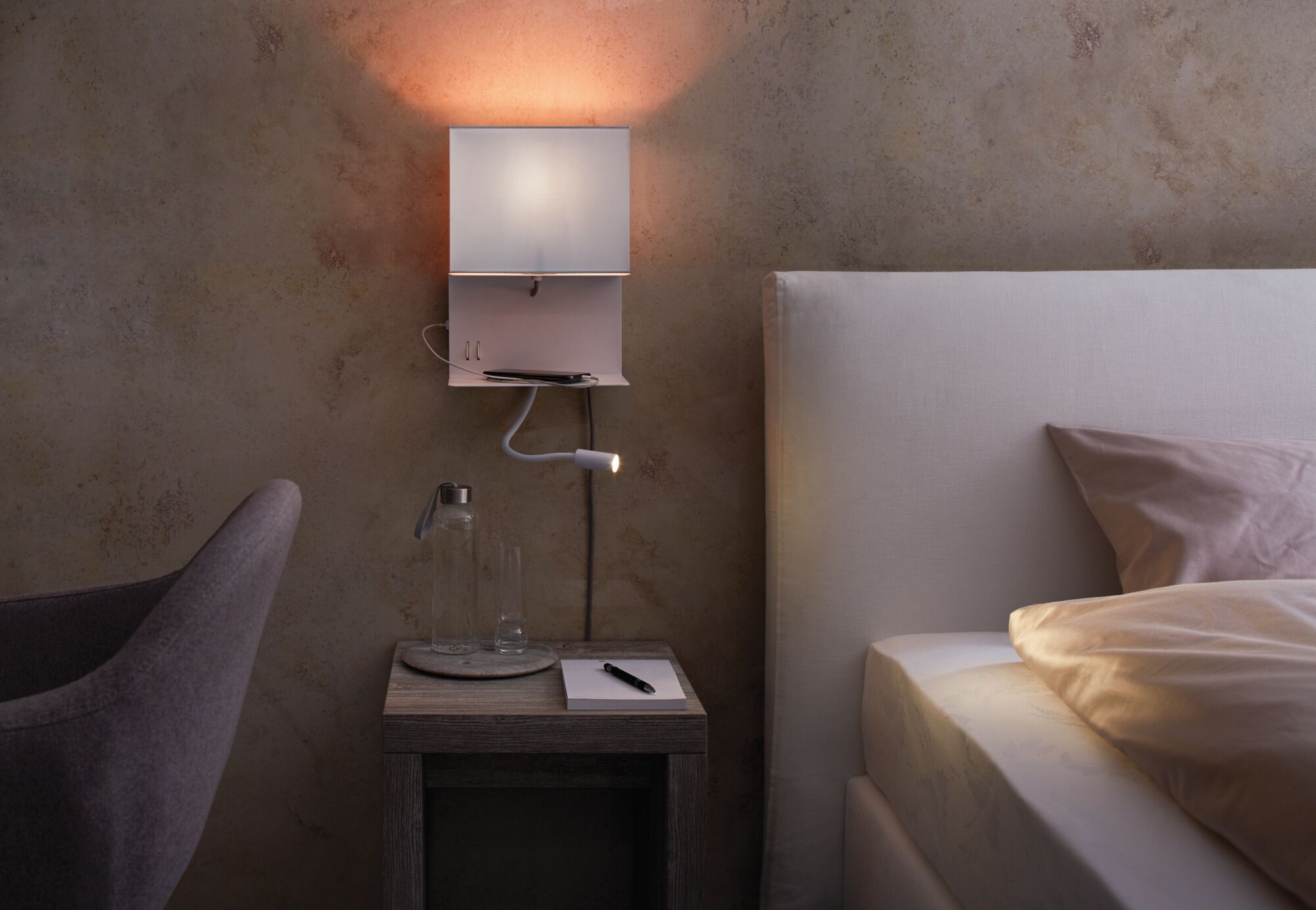 Weißer Wandleser mit flexiblem Lesearm über Nachttisch mit Glasflasche und Notizblock im Schlafzimmer.