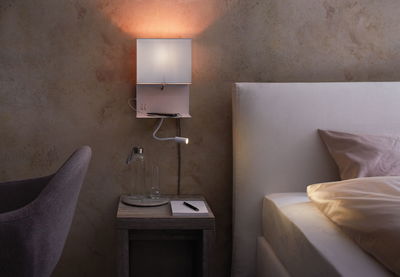 Weißer Wandleser mit flexiblem Lesearm über Nachttisch mit Glasflasche und Notizblock im Schlafzimmer.