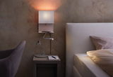 White wall reading lamp with flexible arm above bedside table with glass bottle and notepad in bedroom.