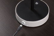 Rundes schwarzes Gerät mit weißem Lederbezug und USB-C-Anschluss auf dunklem Holztisch