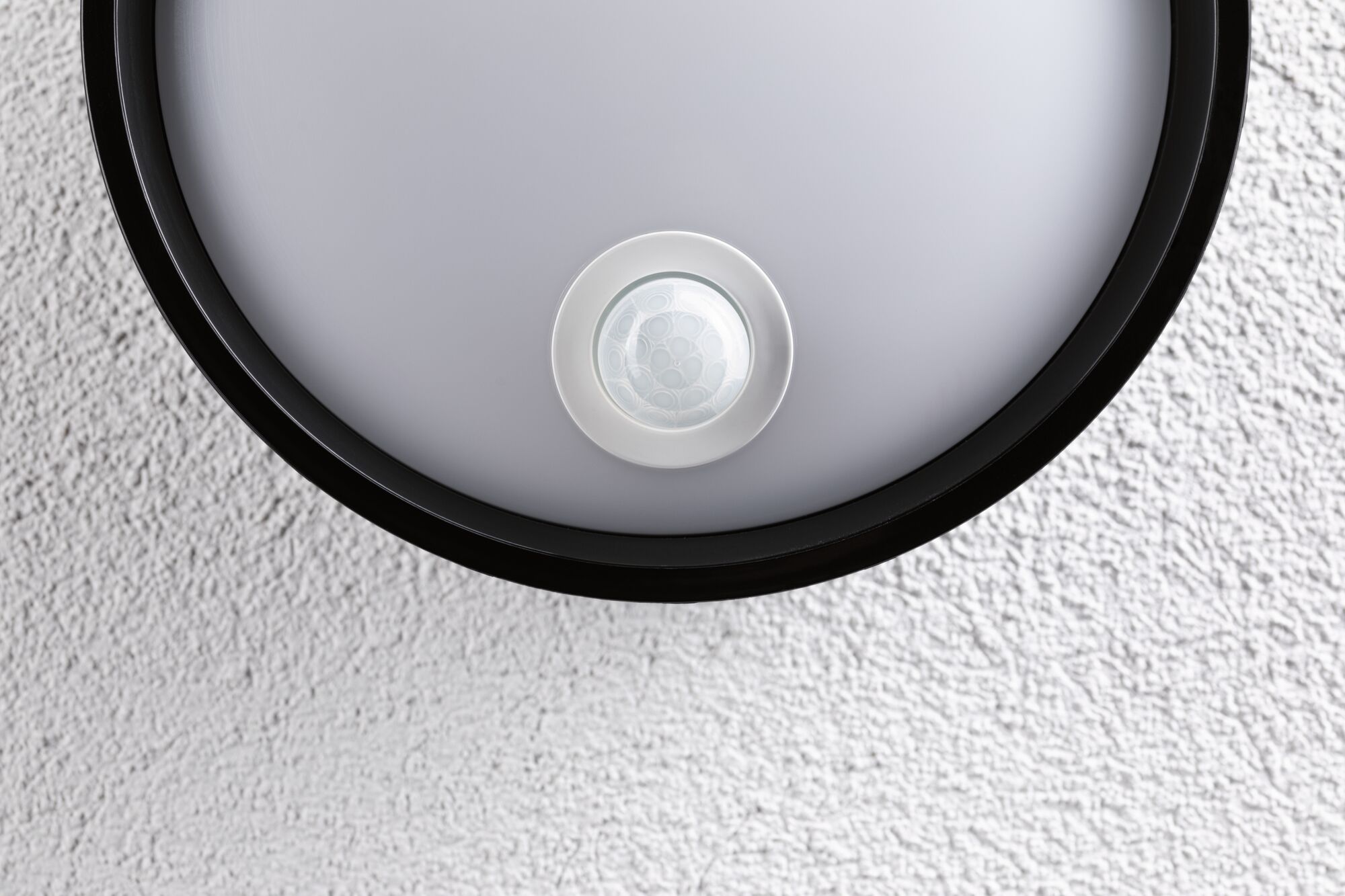 Round ceiling light with black frame and integrated motion sensor on white textured wall