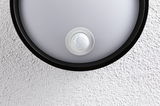 Round ceiling light with black frame and integrated motion sensor on white textured wall