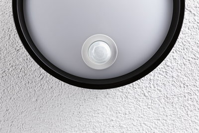 Round ceiling light with black frame and integrated motion sensor on white textured wall
