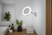 Ronde LED-wandspiegel met chromen metalen arm en warm wit licht in een moderne badkamer.