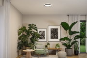 Round ceiling light with white illumination in modern living room featuring green plants and beige armchair.