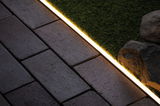 Warmwit LED-striplicht tussen grijze bestrating en groen gras voor buitenverlichting.