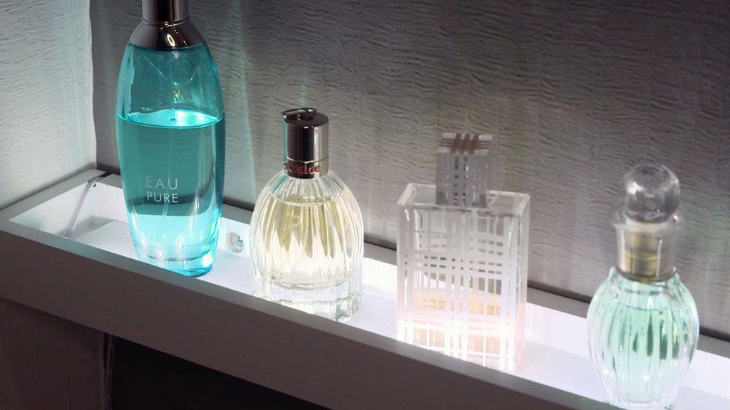 Vier verschiedene Parfümflaschen aus Glas auf beleuchtetem Regal in modernem Badezimmer.