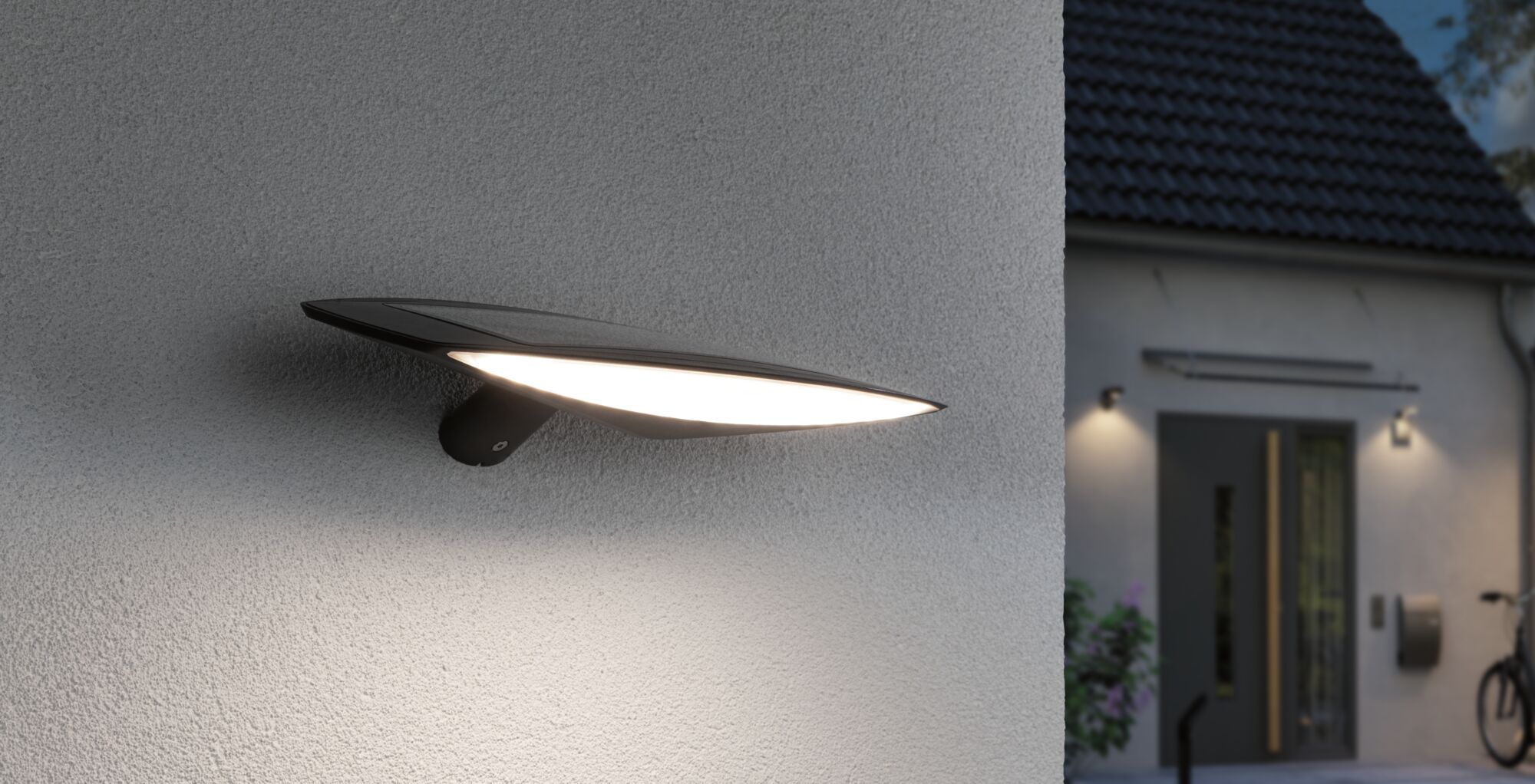 Sort LED udendørs væglampe med bredt lysudslip monteret på husmur til moderne udendørsbelysning