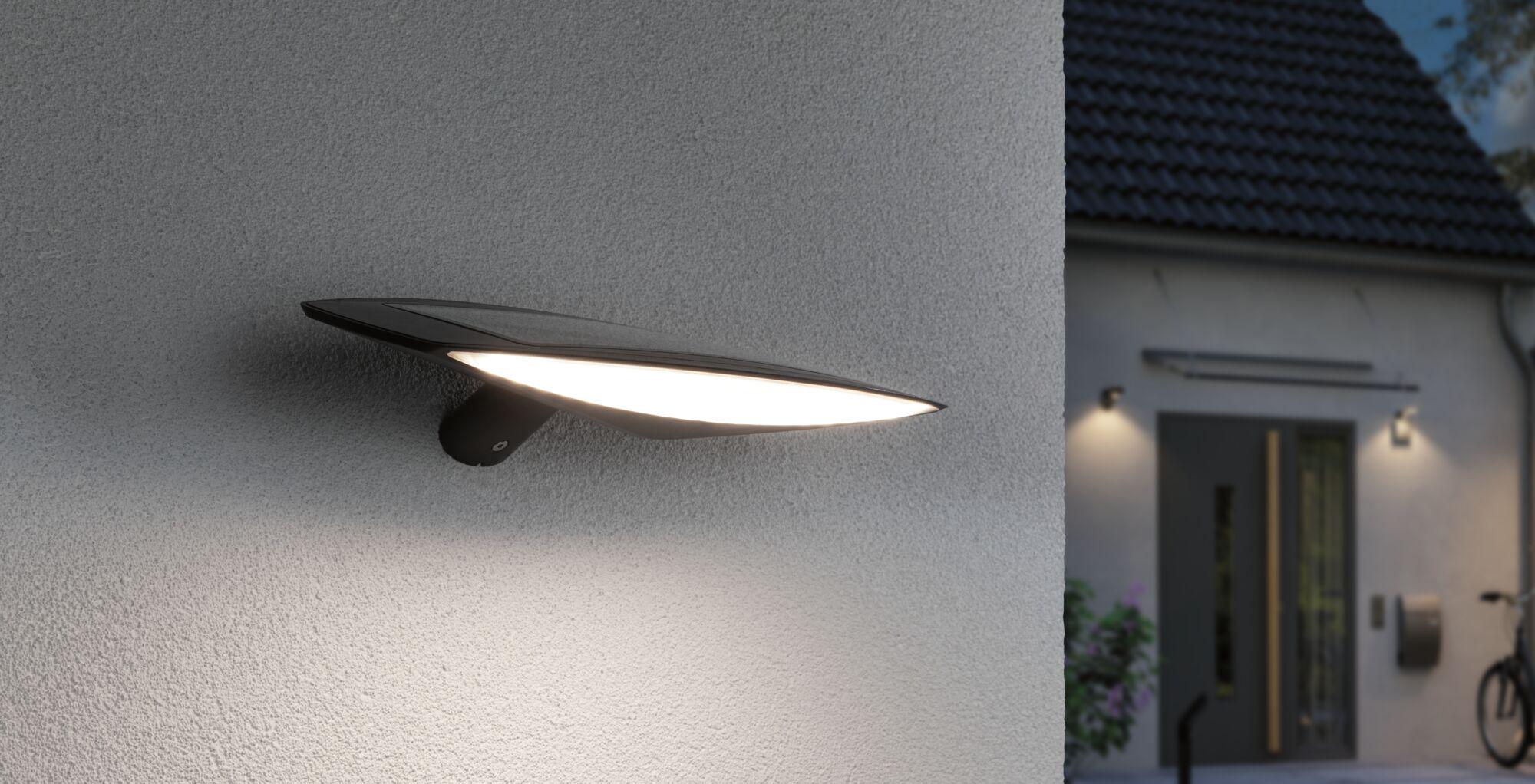 Modern black outdoor wall light with integrated LED and solar panel mounted on house exterior
