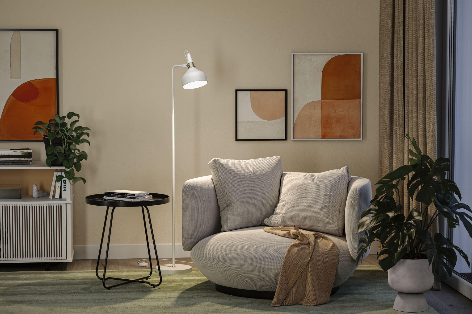 Cozy grey armchair with cushions and throw beside white floor lamp and abstract wall art in living room