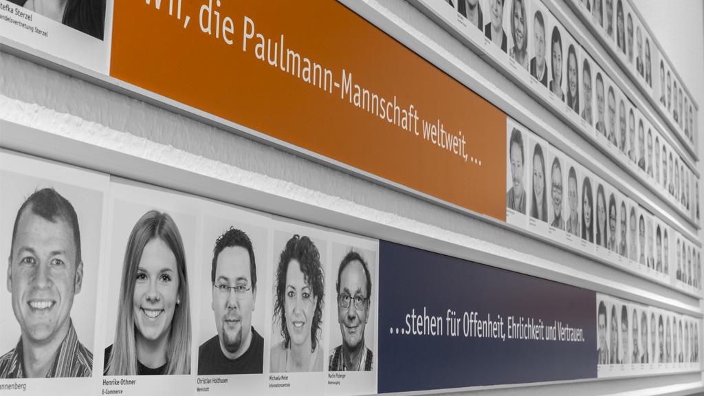 Schwarz-weiß Porträtfotos der Paulmann-Mannschaft an Wand mit Firmenwerten Offenheit und Vertrauen.