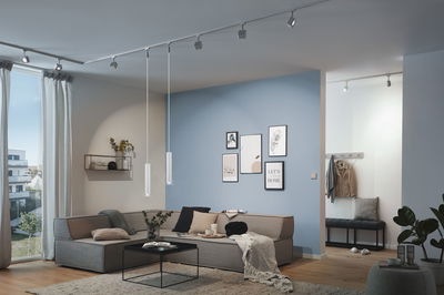 Moderne woonkamer met grijze stoffen bank, blauwe accentmuur en minimalistische LED-plafondverlichting.