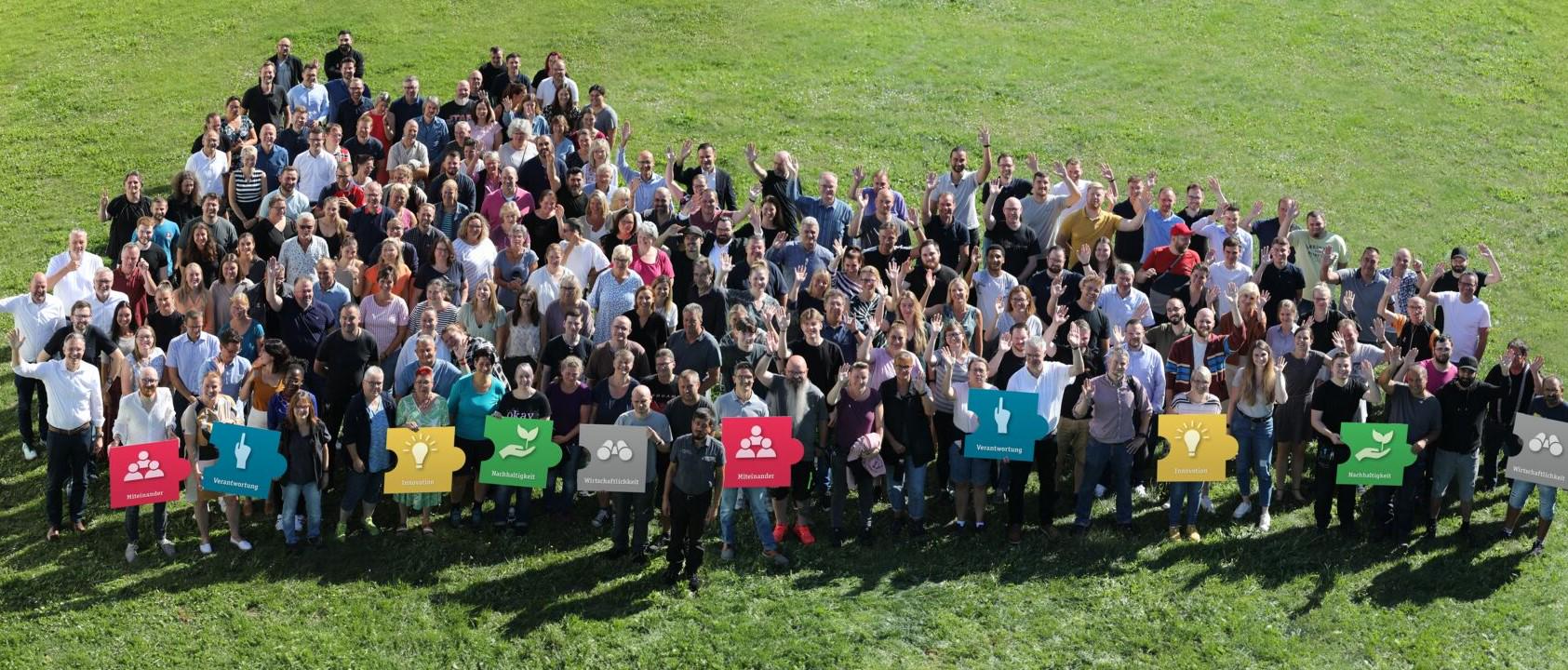 Large group of Paulmann employees on green grass holding signs about company values.