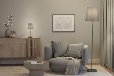 Gemütlicher grauer Sessel mit Kissen und Decke neben grauer Steh- und Tischlampe in modernem Wohnzimmer