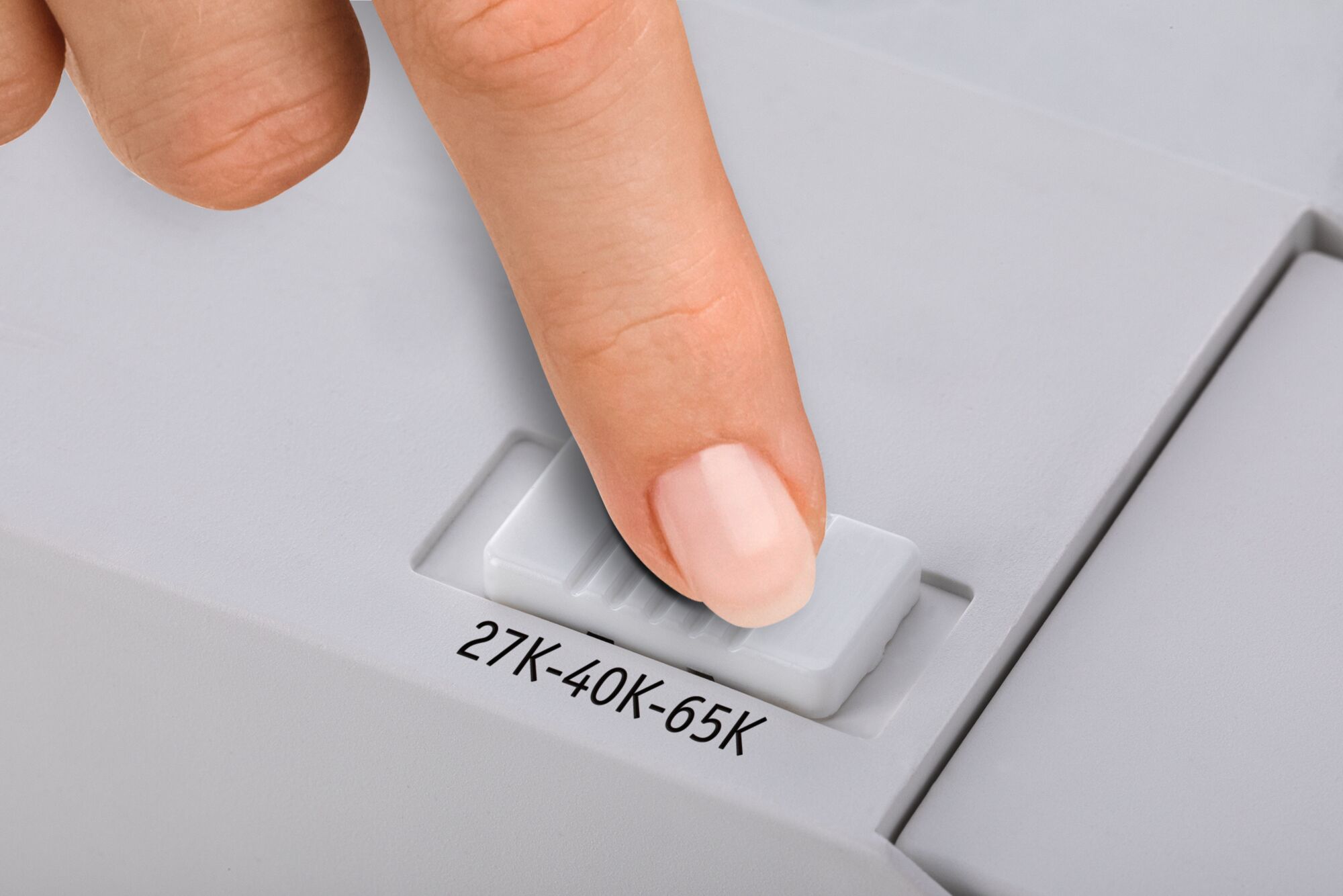 Finger stellt weißen Schieberegler auf einem grauen Gerät mit Beschriftung 27K-40K-65K ein