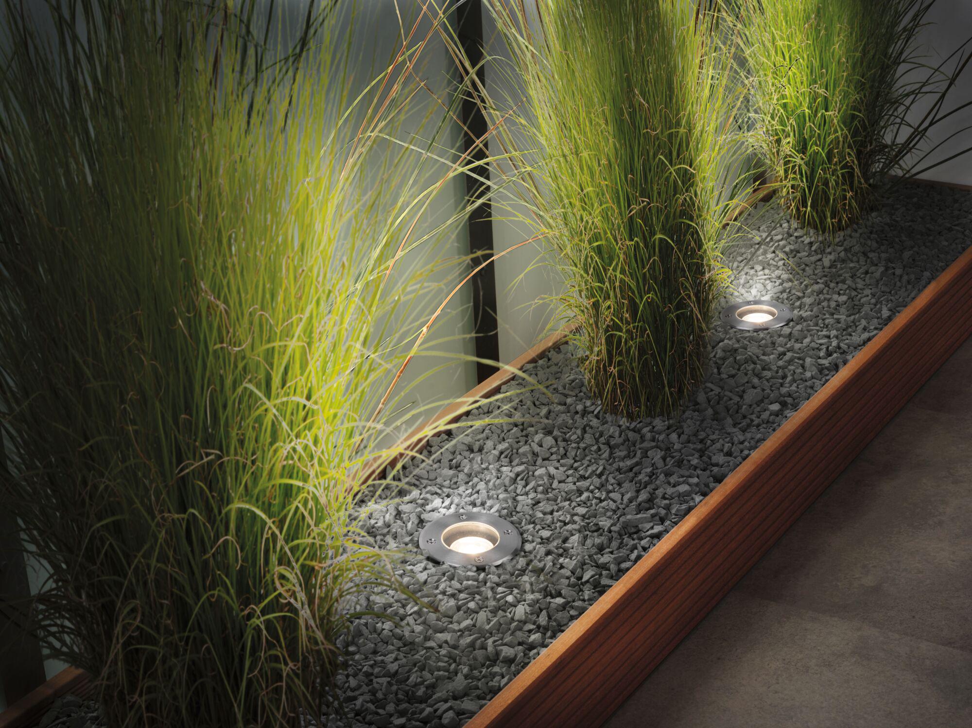Ingebouwde LED-vloerlamp van roestvrij staal in grijze kiezel met groene planten in moderne binnenruimte