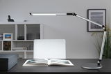 Modern silver metal LED desk lamp with adjustable arm on black desk with open book, office lighting.