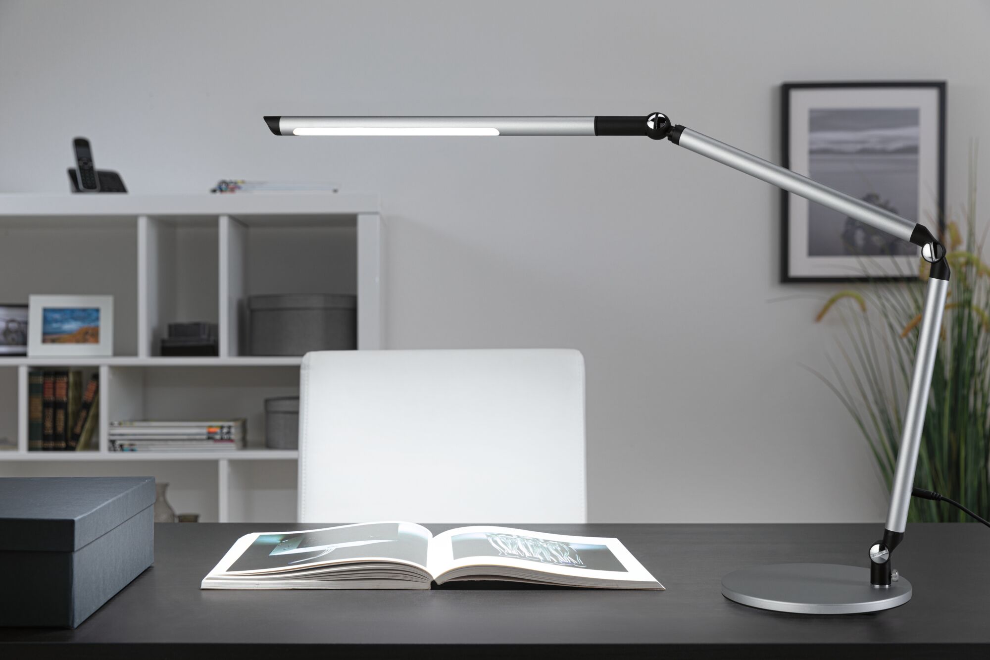 Lampe de bureau LED moderne en métal argenté avec bras réglable sur bureau noir avec livre ouvert.