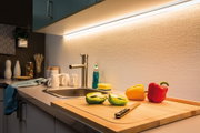 Moderne Küchenarbeitsplatte mit Edelstahlspüle, LED-Unterbauleuchte und bunten Paprikaschoten auf Schneidebrett