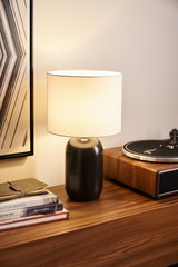 Modern table lamp with black ceramic base and white fabric shade on wooden sideboard with turntable.