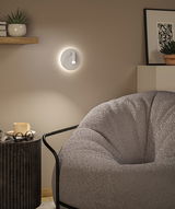Modern white LED wall light with round design on beige wall in living room with grey armchair