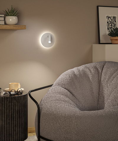 Modern white LED wall light with round design on beige wall in living room with grey armchair