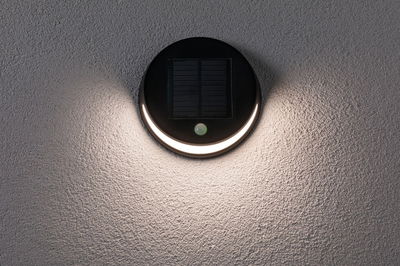 Round black solar wall light with motion sensor and warm white LED on textured grey wall