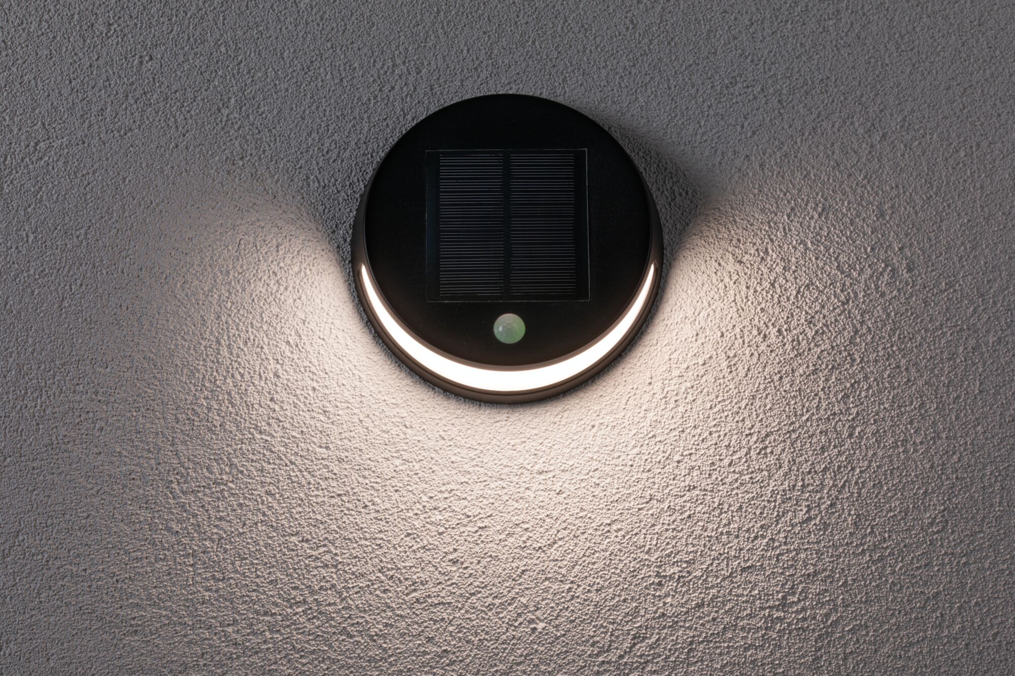 Round black solar wall light with motion sensor and warm white light on textured grey wall