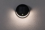 Round black solar wall light with motion sensor and warm white light on textured grey wall