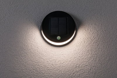 Round black solar wall light with motion sensor and warm white light on textured grey wall