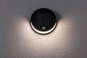 Runde schwarze Solar-Wandleuchte mit Bewegungsmelder und warmweißem Licht an grauer Wand