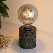 Table lamp with green glass base and large round bulb featuring decorative LED filament light.