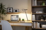 Modern black LED desk lamp with circular light ring on wooden desk in home office setting.