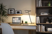 Modern black LED desk lamp with circular light ring on wooden desk in home office setup.