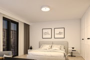 Rundes weißes Deckenlicht aus Kunststoff in modernem Schlafzimmer mit grauem Bett und weißen Wänden.