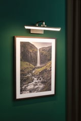 Applique LED moderne en métal brossé sur mur vert pour éclairer des tableaux muraux.