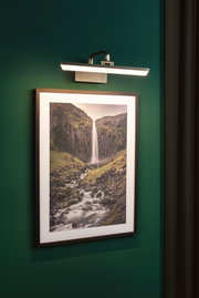 Moderne LED-billedlys i børstet metal på grøn væg til belysning af vægkunst.