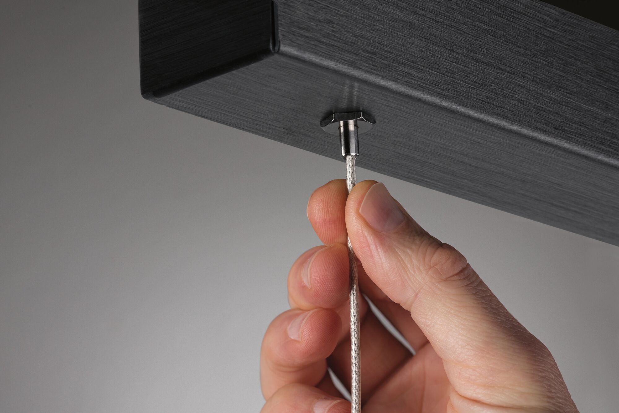 Hand hält weißen Textilkabelanschluss an schwarzem Aluminium-Gehäuse für LED-Beleuchtung