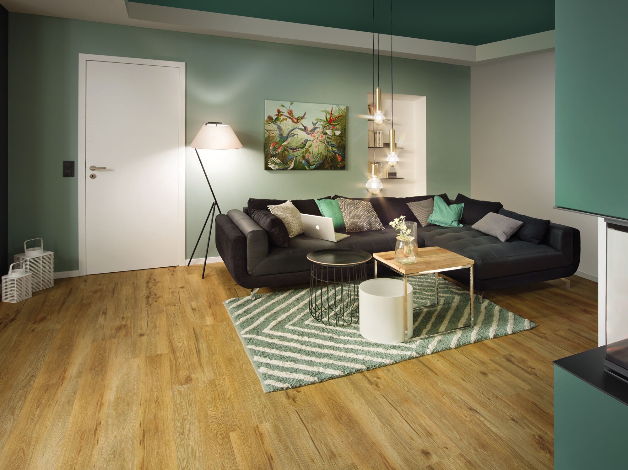Modernes Wohnzimmer mit schwarzem Sofa, grünem Teppich und Holzfußboden in urbanem Dschungel-Stil